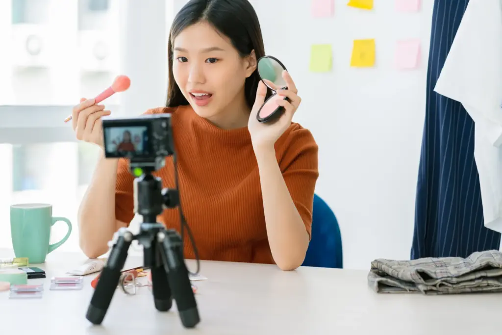 Seorang influencer wanita sedang merekam video tutorial makeup dengan kamera tripod, kegiatan ini salah satu dari strategi influencer marketing